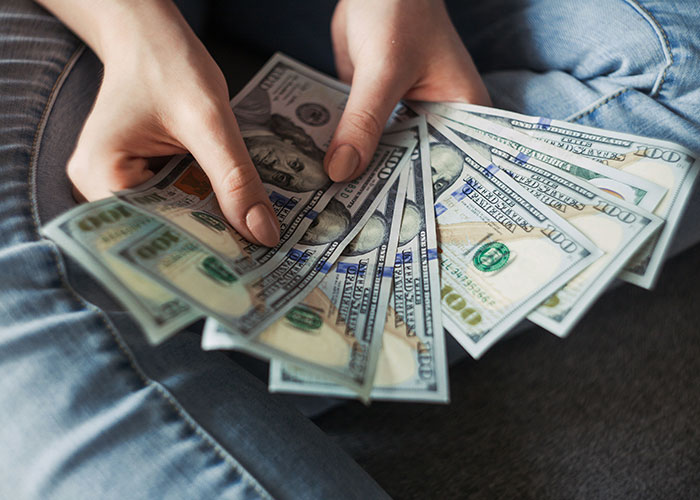 Hands holding multiple hundred-dollar bills, illustrating job descriptions related to manipulate person and product.