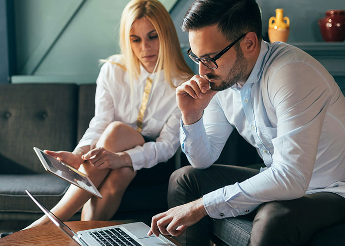 Two professionals collaborating on a product using a laptop and tablet, illustrating hilarious job descriptions.