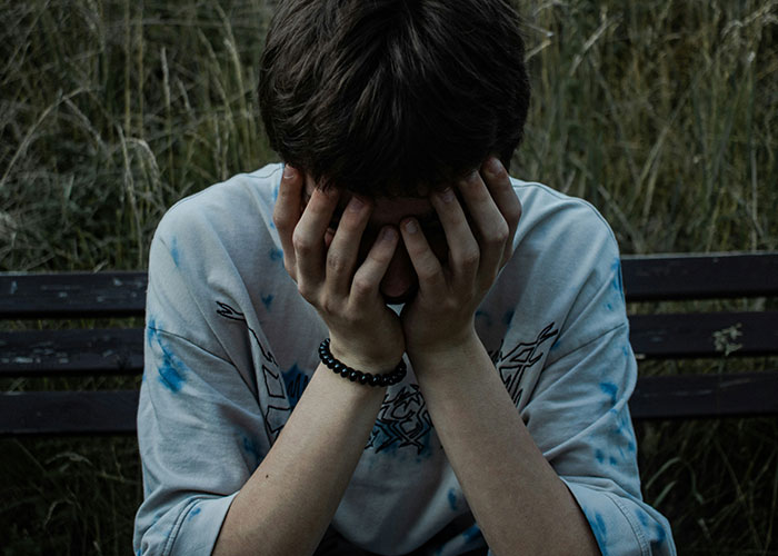 Young person sitting on a bench outdoors, covering face with hands, reflecting on hilarious job descriptions.