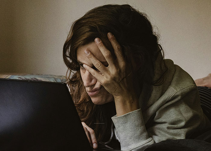 Woman in casual clothes looking frustrated while working on laptop illustrating job descriptions that manipulate person to have product.
