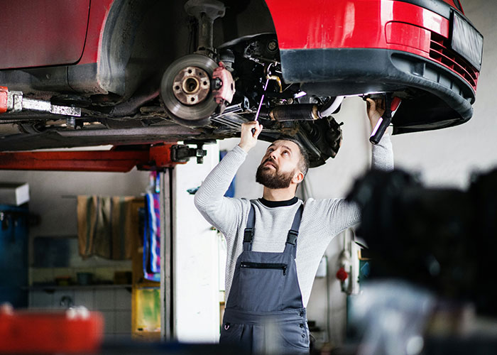 Mechanic inspecting car suspension in a workshop, highlighting a humorous job description about product manipulation.