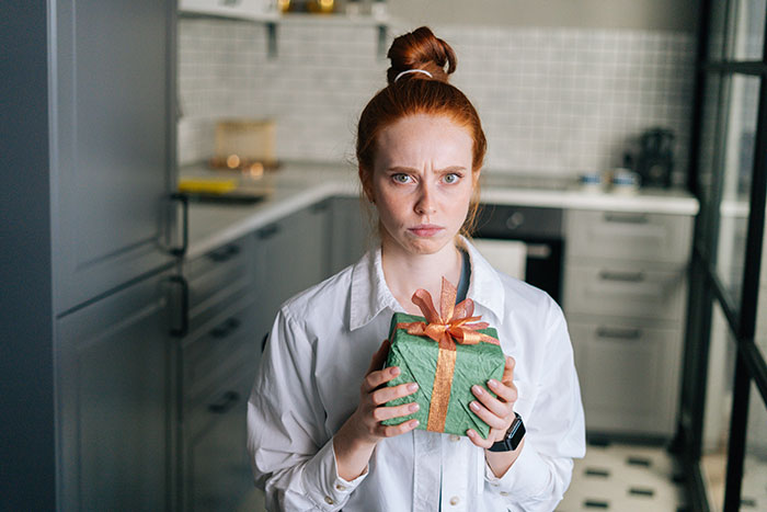 Woman looking horrified holding a wrapped anniversary gift from a guy who considers her his girlfriend after one date