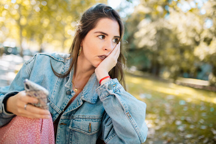 Young woman in a denim jacket looking worried and distracted outdoors, experiencing creepy and scary situations feelings.