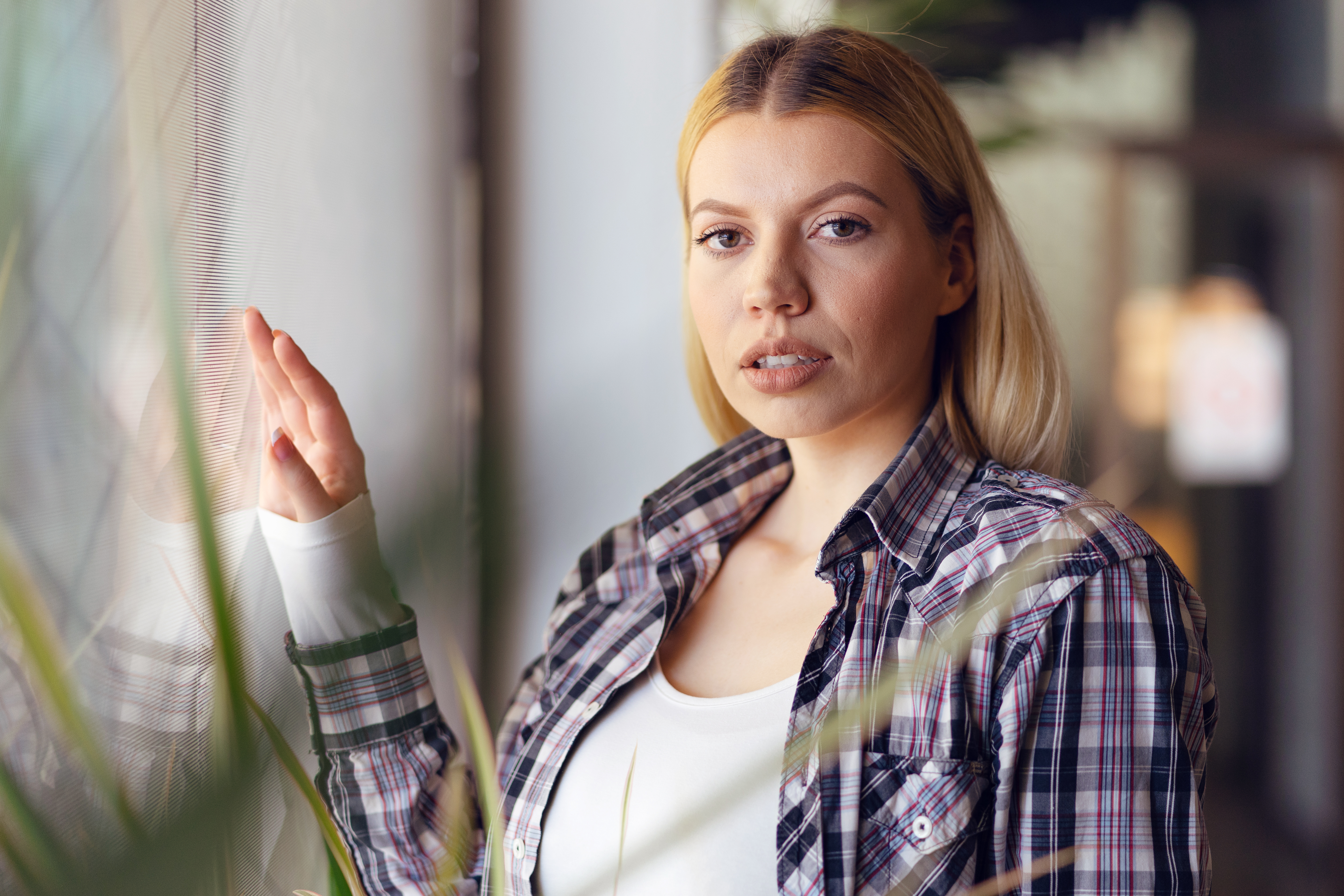 Young woman in a plaid shirt looking serious, reflecting on family demands about giving her baby to her sister.