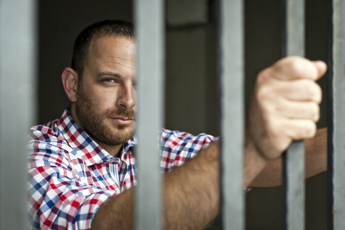 Man wearing checkered shirt gripping prison bars, representing the darkest family secrets people found out.