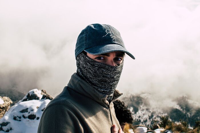 Person in outdoor gear wearing a cap and face covering, looking cautiously in a scary creepy situation setting.