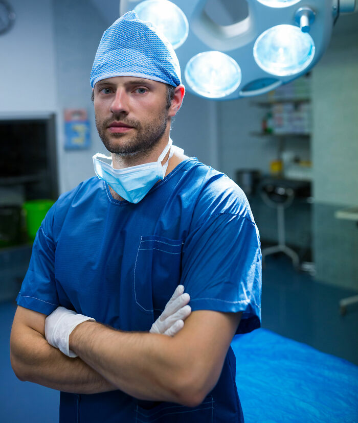 Surgeon in scrubs and gloves standing with arms crossed in an operating room, representing professions not seen as relationship material.