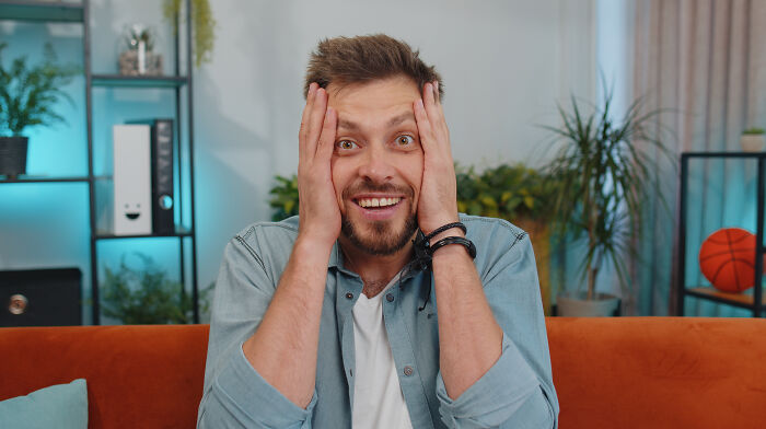 Man with a shocked expression sitting on an orange couch, illustrating sewer workers seeing bizarre things while working down there.