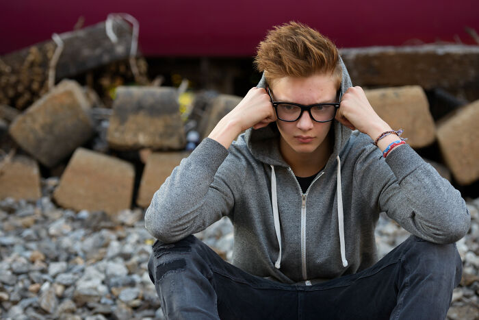 Teen wearing glasses and a gray hoodie sitting among rocks looking worried after people saw scary creepy situations.