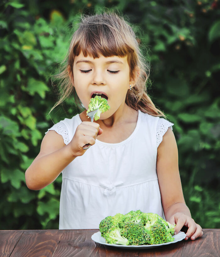 Young girl eating broccoli outdoors, demonstrating parenting hacks to encourage healthy eating and save sanity.