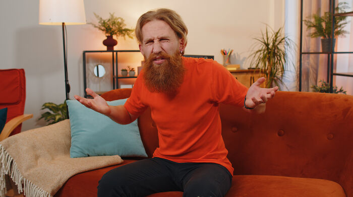 A confused man sitting on an orange couch expressing frustration while illustrating common red flags in dating scenarios.