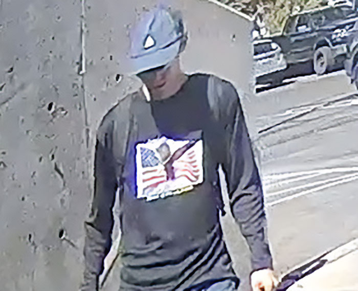 Bearded man in crowd wearing hat and patriotic shirt, spotted cheering and looking back during Charlie Kirk incident.