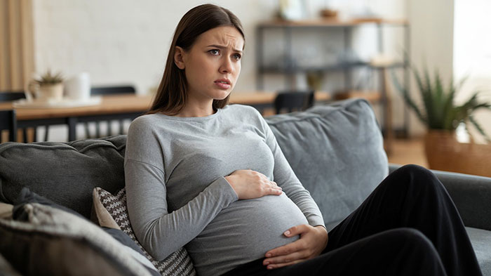 Pregnant woman looking worried on couch risking anaphylaxis as sister-in-law ignores no-peanut allergy rule at home. Pregnant woman looking worried on couch risking anaphylaxis as sister-in-law ignores no-peanut allergy rule at home.