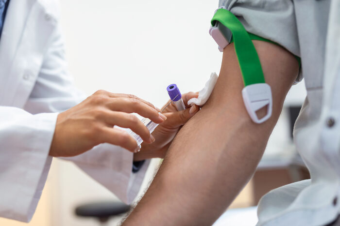 Doctor preparing to draw blood from patient's arm using a needle and tourniquet in a clinical setting.