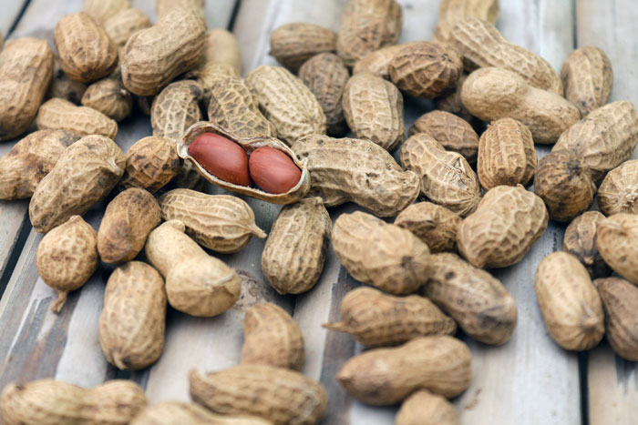 Close-up of peanuts in shells scattered on a wooden surface, highlighting peanut allergy risk in food theft incidents.