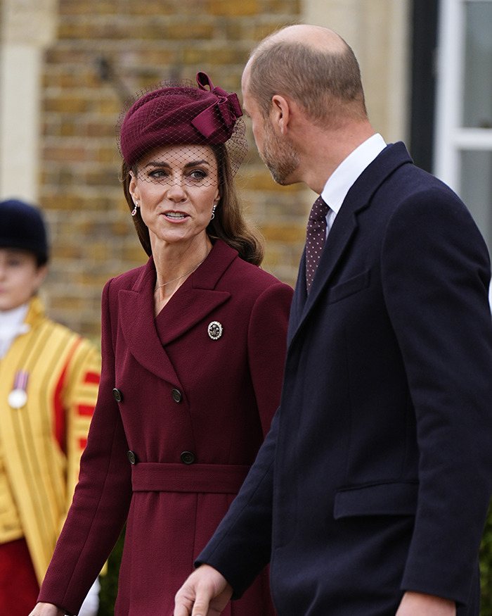 Kate Middleton in a burgundy coat and hat speaking with Prince William outdoors, related to Princess Charlotte&rsquo;s curtsy mistake.