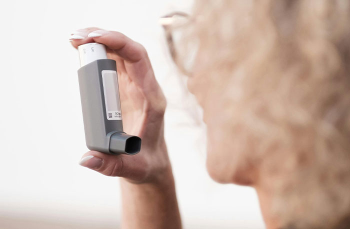 Woman with curly hair holding an asthma inhaler close to her face showing medical accuracy from House M.D. diagnoses.