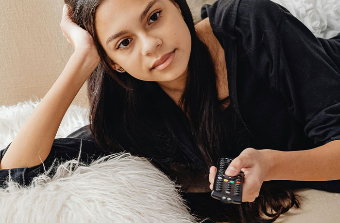 Young woman lying on couch with TV remote, representing doctors discussing accurate and inaccurate diagnoses from House M.D.