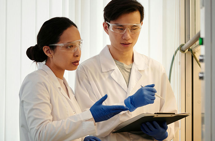 Two doctors in lab coats and safety glasses discussing accurate medical diagnoses in a clinical research setting.
