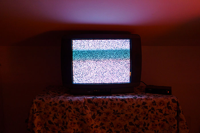 Old TV showing static and distortion on a floral-covered table in a dark room, evoking scary real-life stories.