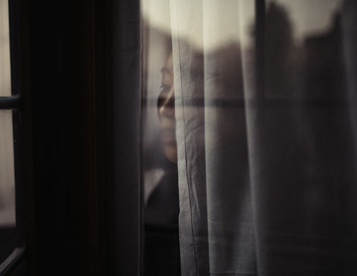 Woman's faint reflection behind curtain in dim light, evoking eerie and scary real-life stories mood.