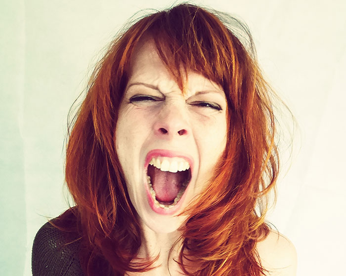 Woman with red hair screaming with eyes closed, expressing fear and shock in a scary real-life story moment.