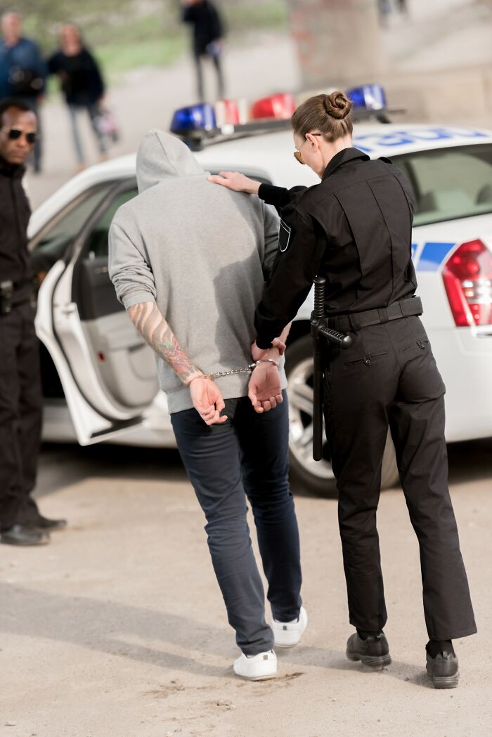 Police officer arresting a suspect in handcuffs near a patrol car, highlighting innocent people blamed by police.