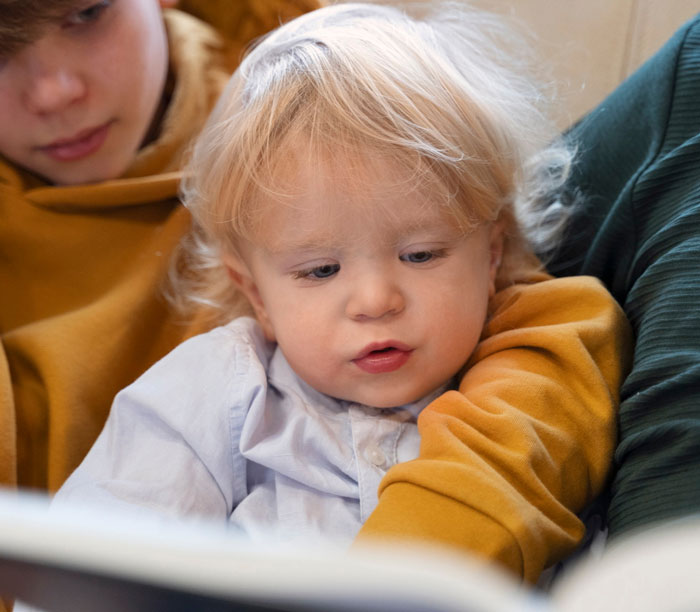 Older sibling reading to a toddler stepsibling, illustrating family moments related to refusing babysit stepsiblings.