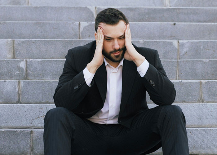 Man in suit sitting on stairs with hands on head, looking stressed over naming baby after first girlfriend and upsetting wife Man in suit sitting on stairs with hands on head, looking stressed over naming baby after first girlfriend and upsetting wife