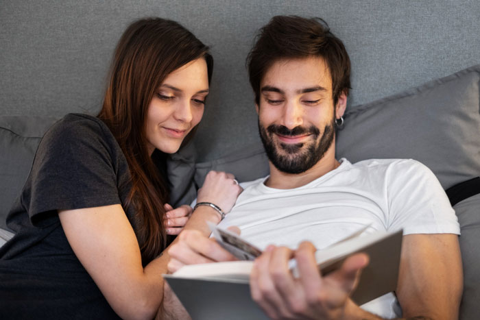 Young man and woman relaxing together while looking at a book, reflecting on refusing to watch autistic friends show recommendations.