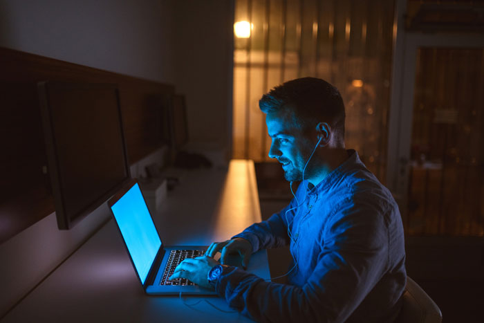Man in blue shirt uses laptop at night, reflecting on online affair and guilt after ruining marriage.