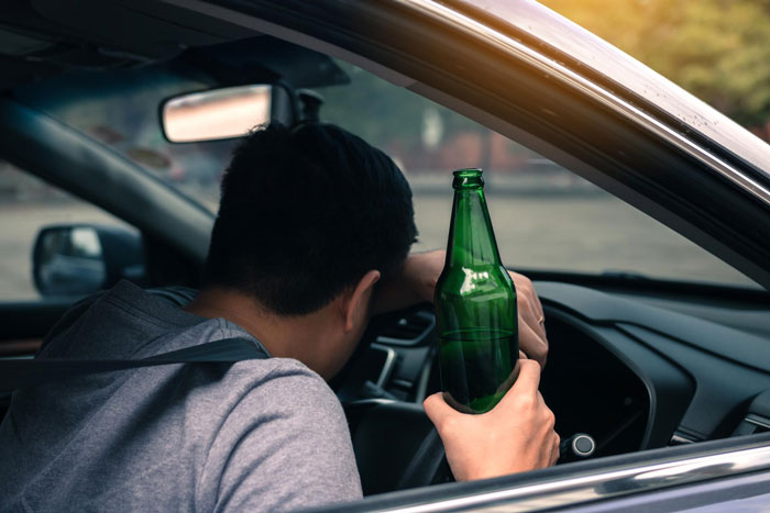 Young man holding a beer bottle inside a car, related to reporting drunk driver and curfew violation ticket incident.