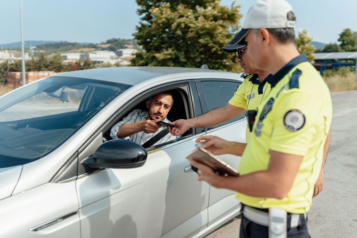 Young driver handing ID to police officers during a roadside check involving a curfew violation ticket.