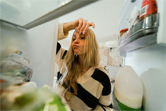Woman looking frustrated inside an overcrowded office fridge, struggling to find space for her lunch. Woman looking frustrated inside an overcrowded office fridge, struggling to find space for her lunch.