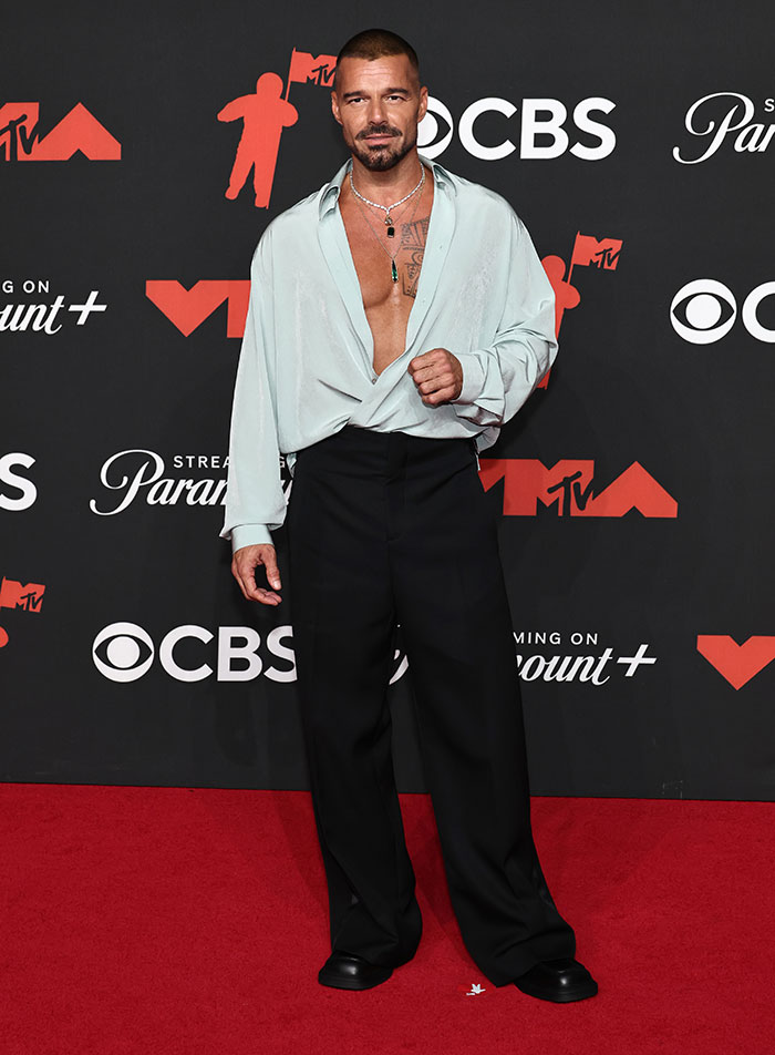 Male celebrity on the red carpet wearing a loose, open shirt and black pants at the worst dressed stars 2025 Video Music Awards.