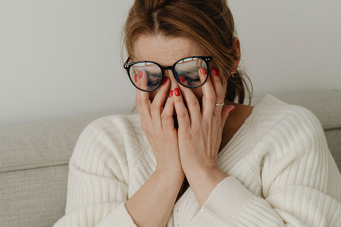 Woman in glasses covering her face with hands, showing frustration and stress, depicting maddening reasons men got upset at women.