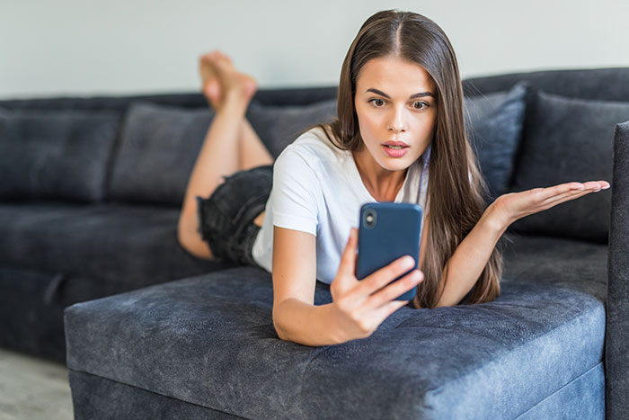 Young woman lying on a couch looking upset at her phone, depicting maddening and illogical reasons men got upset at women.