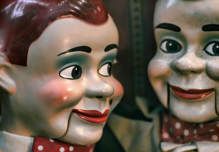 Two vintage ventriloquist dummies with painted faces, highlighting the unusual combination of butcher and gravedigger professions.