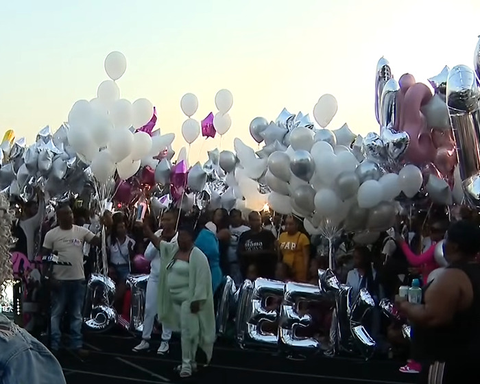 Community gathers at a vigil holding white and silver balloons in memory of a mom fatally shot after dropping off her son.