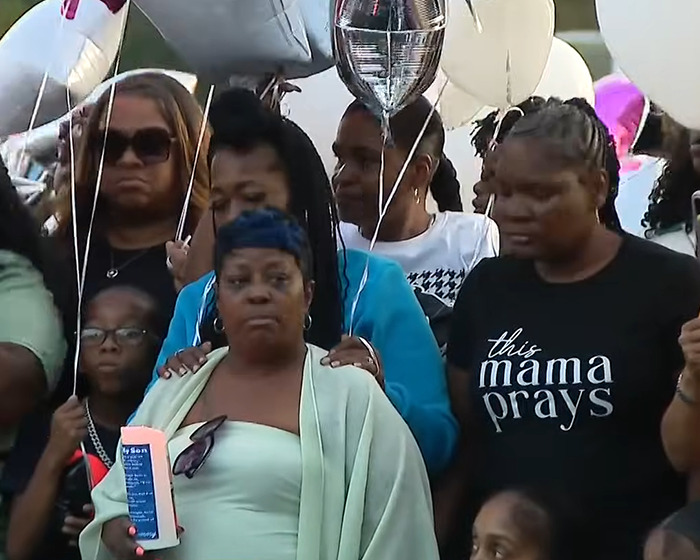 Group of grieving people holding balloons at a vigil honoring a mom fatally shot after slipping a loving note in her son&rsquo;s lunchbox