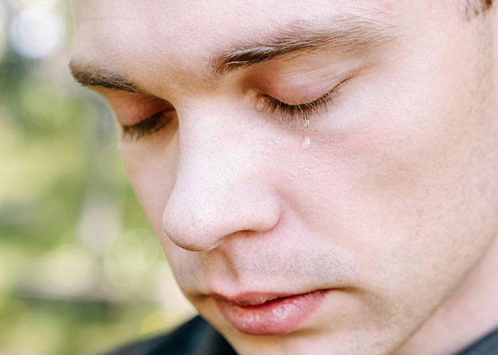 Close-up of a man with eyes closed and a tear rolling down, expressing emotional breakdown and vulnerability.