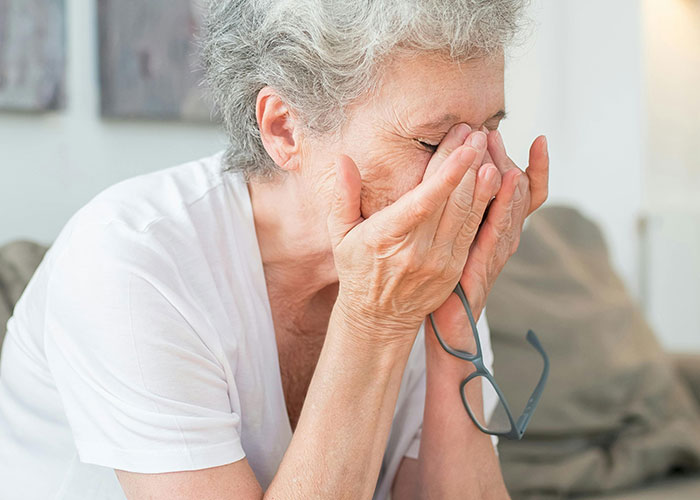 Older woman holding glasses and covering her face, reflecting years of rude comments impacting family emotions.