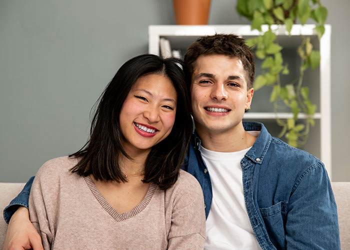 Happy couple sitting together on a couch, smiling and showing support amid years of rude comments from mother-in-law.