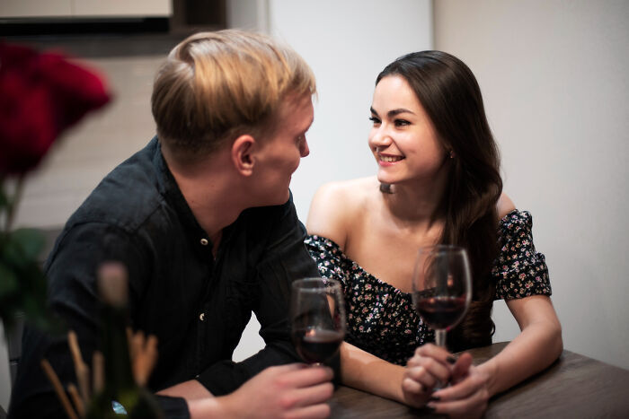 A young couple sharing a first date, holding wine glasses and smiling, illustrating ways to ruin a first date scenario.