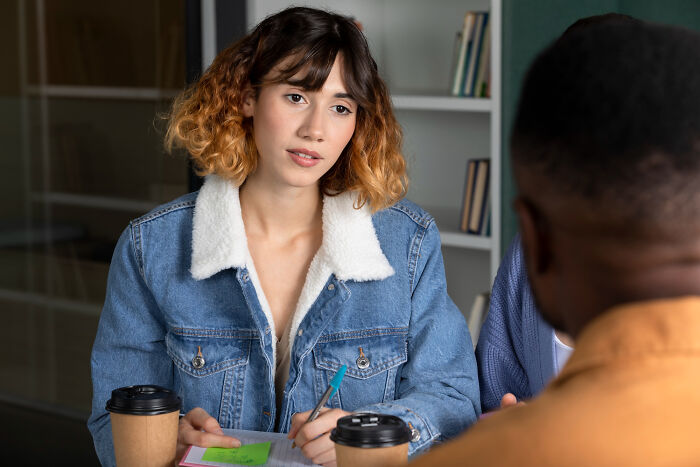 Young woman in denim jacket on a first date, discussing and taking notes while talking to her date in a cafe setting.