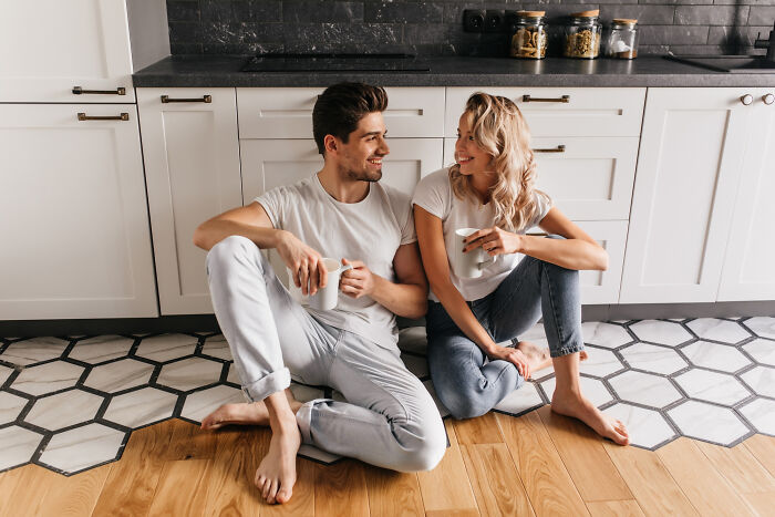 Young couple sitting on kitchen floor, enjoying coffee and smiling, illustrating funny ways to ruin a first date quickly.