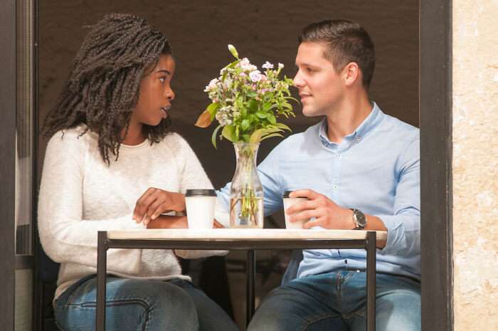 Couple on a first date at a cafe with coffee cups and flowers, illustrating ways to ruin a first date quickly.