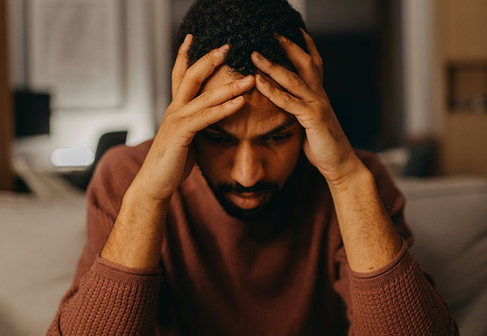 Man looking stressed and overwhelmed, holding head in hands, illustrating unintended life impact or missing person concerns.