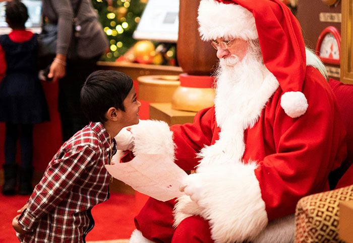 Child talking to Santa Claus in red suit, sharing a note, capturing a festive and heartfelt moment.