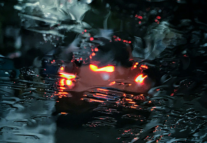 Blurred car lights at night seen through rain-covered glass, capturing a moody scene related to missing person stories.